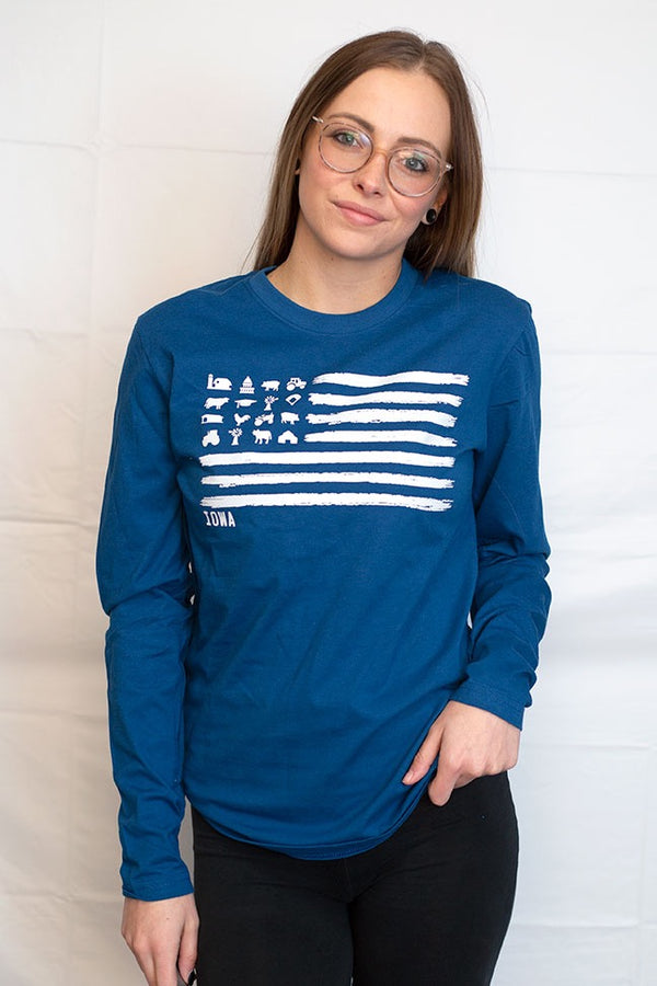 A woman wearing a Cool Blue colored, unisex, 100% cotton long sleeved tee shirt. Light Grey front graphic mimics a flag design with barns, tractors, silos, animals in the stars field . Available in sizes small to 3X-Large.