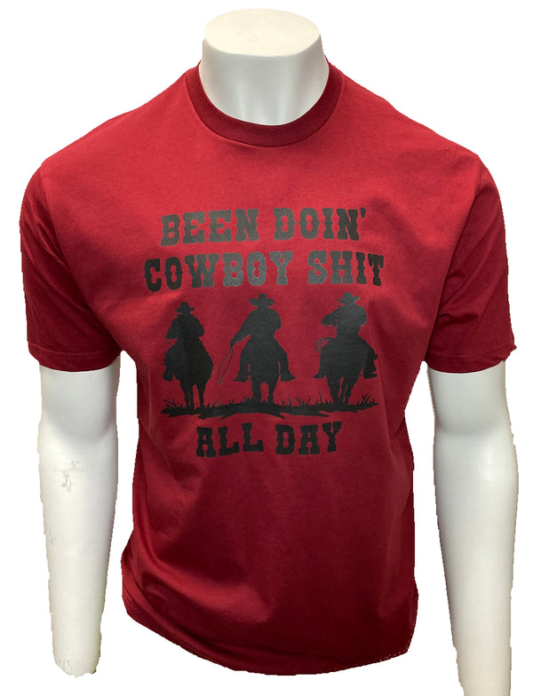 Red tee shirt with short sleeves. Silhouette of Cowboys on horses reads Been Doin' Cowboy Shit All Day.