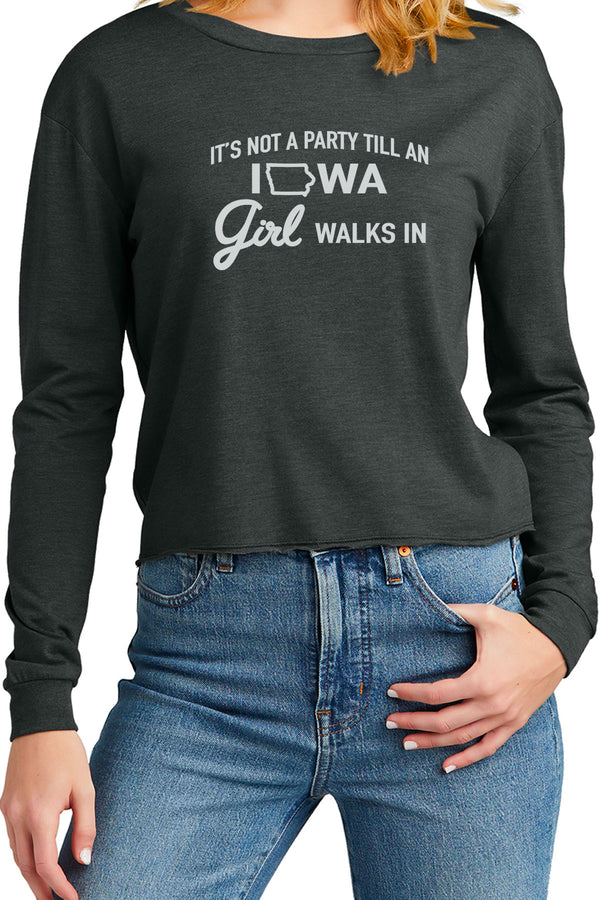 Woman wearing a long sleeved tee that is cropped below the belly button. Shirt color is Black Frost. Crew neck, cuffs on sleeves, surged hem at bottom of shirt. Front white graphic reads, It's Not A Party Till An Iowa Girl Walks In. Cotton, polyester, rayon blend shirt. Sizes  Extra small to 3 XL.