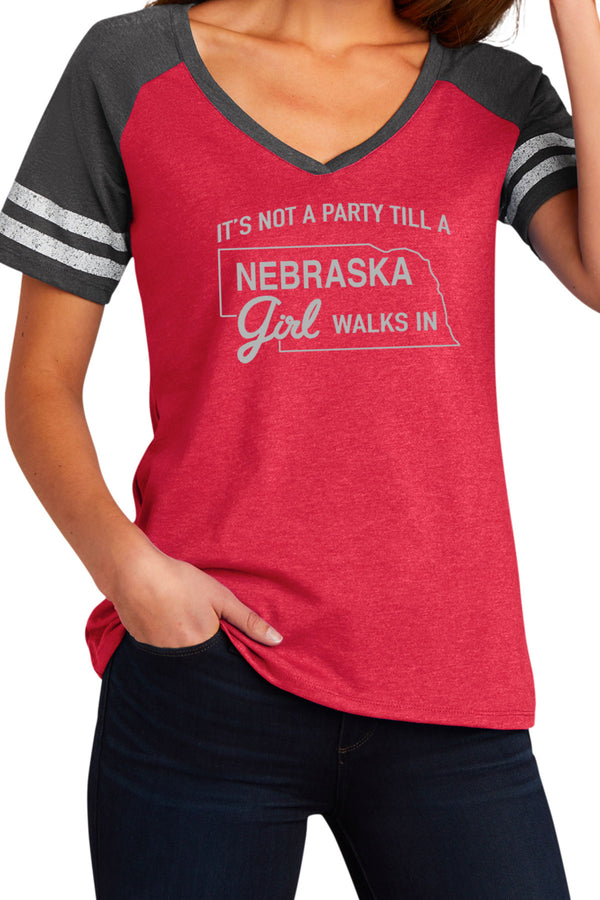 Woman wearing a game day styled, V neck short sleeved tee shirt. Red shirt, grey sleeves, two white stripes on each sleeve. Front white graphic reads It's Not A Party Till A Nebraska Girl Walks In. Sizes small to 3X-Large.