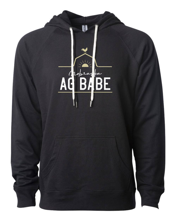 A mannequin wearing a unisex, black pouch front hooded sweatshirt. A front graphic in gold and white shows a barn roof line, rooster and sun with sun rays. Just under the roof line large lettering reads Nebraska Ag Babe  