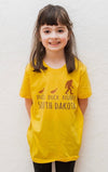 A Heather Yellow Gold short sleeved toddler and youth sized shirt. The front graphic shows two ducks following Bigfoot. The design is called Duck Duck Bigfoot South Dakota.