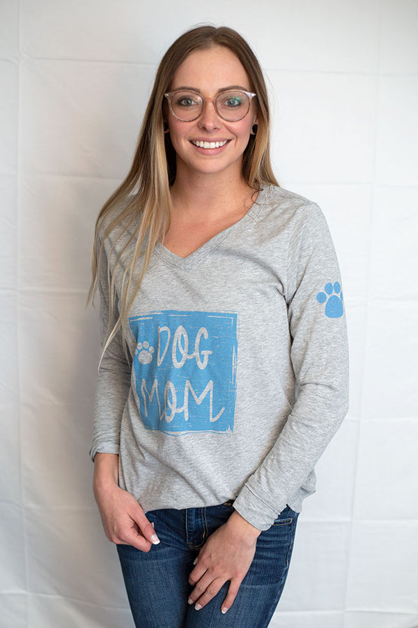 A Light Grey Heather V-neck long sleeved tee. DOG MOM with paw prints front graphic in light blue. Paw print on left sleeve. Sizes small to 4X-Large