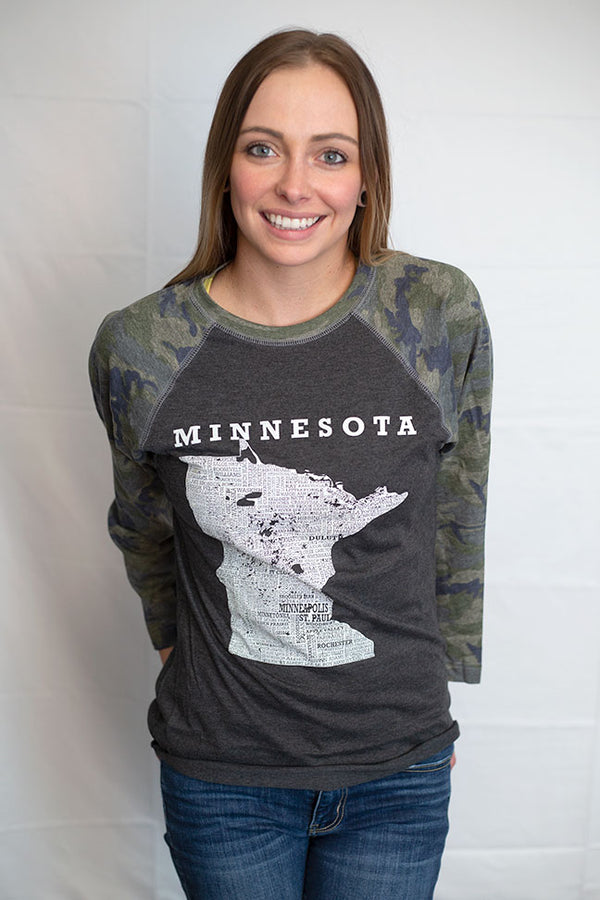 A woman wearing a Dark Grey Heather, Camo sleeved unisex baseball tee with raglan sleeves. On the shirt front is a light grey graphic of the state of Minnesota and its cities. Sizes small to 3X-Large. A Scratchpad  Tees original design.