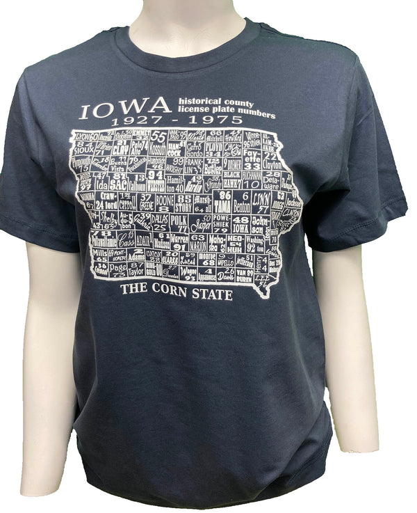 A female mannequin wearing a Steel Blue, unisex, 100 percent cotton, short sleeved tee. The white front graphic is a map of Iowa counties with historical number and name. Wording reads Iowa, The Corn State. Available in sizes Small to 3 X-Large