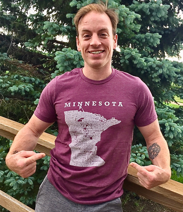 A man wearing a unisex sized, Heather Maroon crew neck, cotton polyester, short sleeve tee. Front white graphic is of Minnesota and its cities. Sizes small to 3X-Lagre. A Scratchpad Tees original design.
