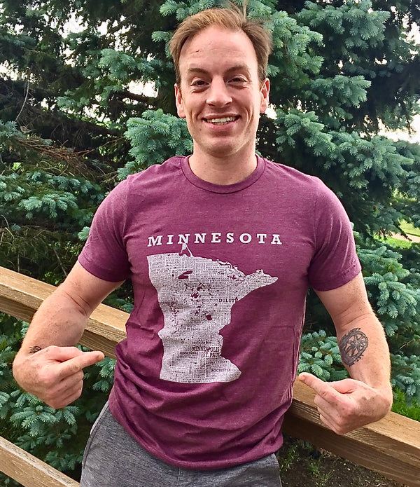 A man wearing a unisex sized, Heather Maroon crew neck, cotton polyester, short sleeve tee. Front white graphic is of Minnesota and its cities. Sizes small to 3X-Lagre. A Scratchpad Tees original design.