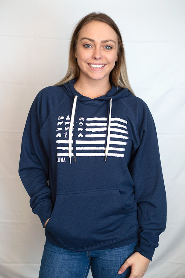 A woman wearing an Indigo colored, unisex, pouch front, Loopback Terry hooded sweatshirt. Light Grey front graphic mimics a flag design with barns, tractors, silos, animals in the stars field. Contrast drawstrings. Available in sizes small to 3X-Large.