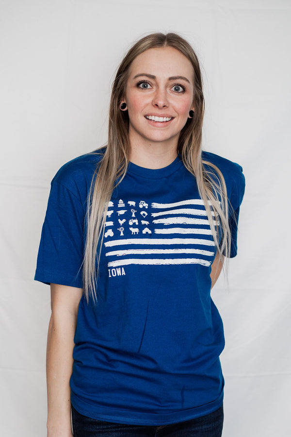 A woman wearing a Cool Blue colored, unisex, 100% cotton short sleeved tee shirt. Light Grey front graphic mimics a flag design with barns, tractors, silos, animals in the stars field . Available in sizes small to 3X-Large.