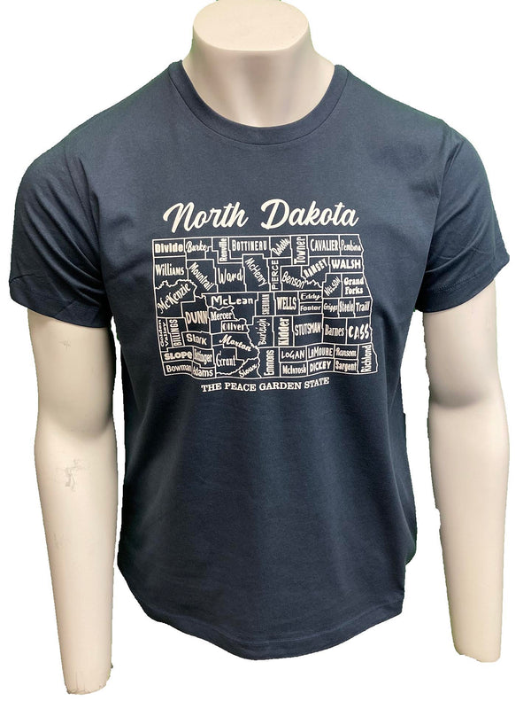 A male mannequin wearing a Steel Blue, unisex, 100 percent cotton, short sleeved tee. The white front graphic is a map of North Dakota counties by name. Wording reads North Dakota The Peace Garden State. Available in sizes Small to 3 X-Large