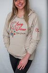 A Sand colored mid-weight hooded sweatshirt with pouch front. A colorful dream catcher and message on shirt front. Front reads Living The Dream North Dakota.