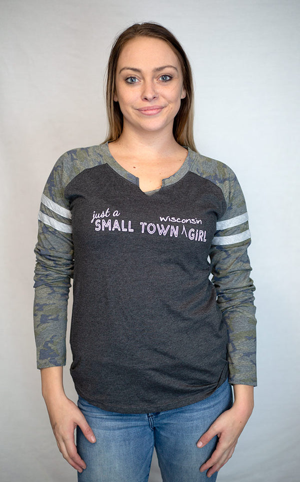 A ladies cut long sleeve notched collar jersey styled tee shirt. Dark grey body with Camo sleeves . Front white graphic says Just A Small Town Wisconsin Girl .