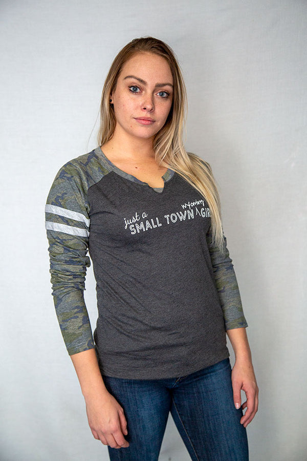 A ladies cut long sleeve notched collar jersey styled tee shirt. Dark grey body with Camo sleeves . Front white graphic says Just A Small Town Wyoming Girl .