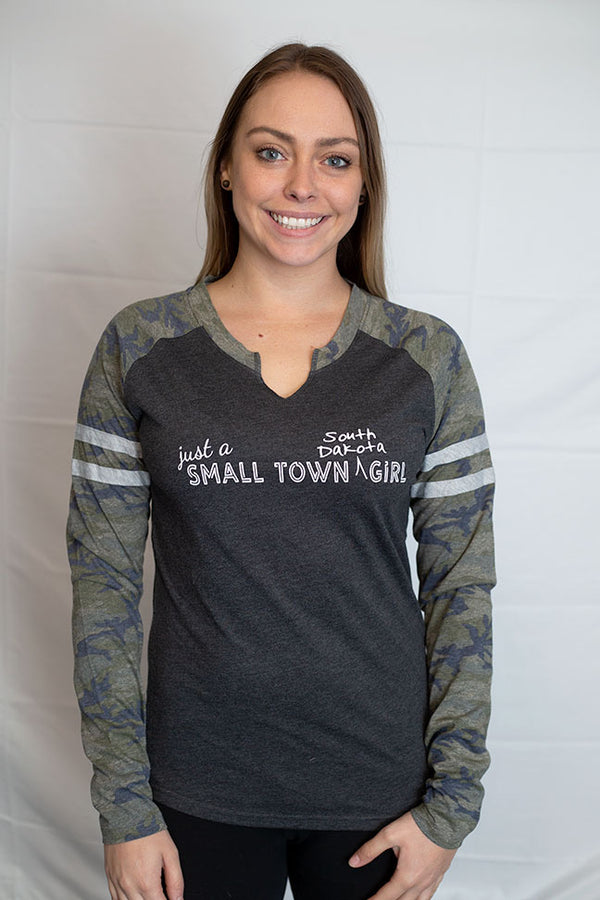 A ladies cut long sleeve notched collar jersey styled tee shirt. Dark grey body with Camo sleeves . Front white graphic says Just A Small Town South Dakota Girl .