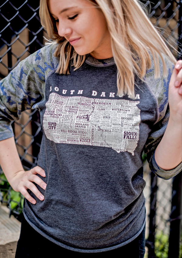 A Dark Grey Heather, Camo sleeved baseball tee with raglan sleeves. Front light grey graphic shows South Dakota and 95% of its cities. Sizes small to 3X-Large. A Scratchpad Tees original design.